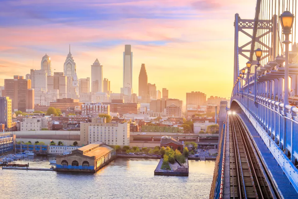 Phialdelphia skyline at sunset with close-up of bridge in foreground.
